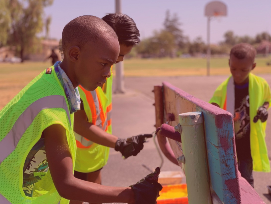 Three youth of color paint a park bench